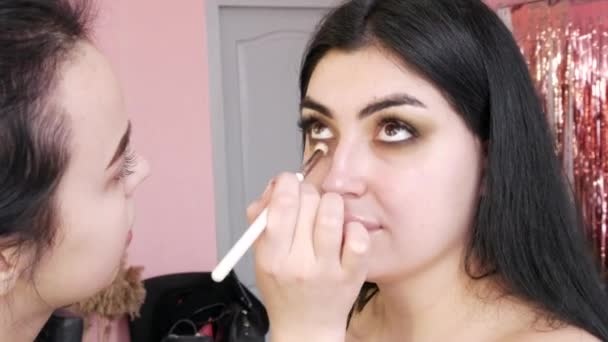 Дівчина-стиліст робить макіяж для красивої моделі жінки, використовуючи спеціальний пензлик для макіяжу очей — стокове відео
