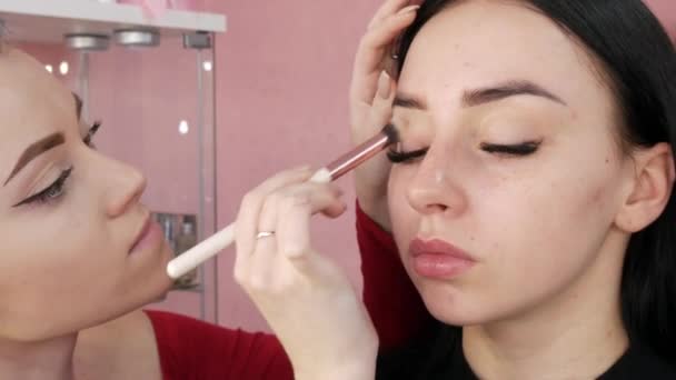 Chica estilista maquillaje artista aplica la fundación bajo la fundación con un cepillo especial en la cara de la chica modelo — Vídeos de Stock