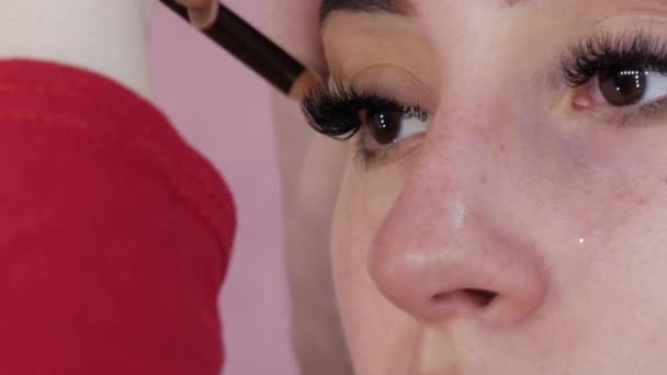 Big long false eyelashes of a young female model. A special eyeliner pencil draws a shaded arrow in the eye makeup — Stock Video