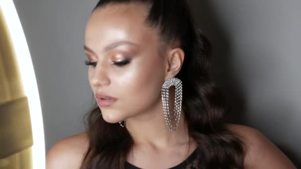 Modelo de menina bonita com um penteado de rabo de cavalo alto e brincos de strass maciços. Alta moda posando com noite elegante compõem olhos fumegantes. Extensões de pestanas longas e maquiagem para os olhos — Vídeo de Stock