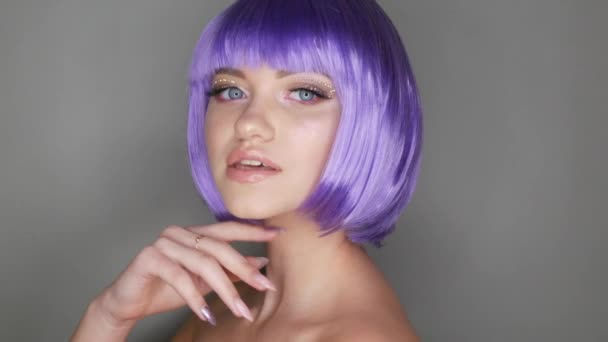 Bella giovane ragazza modello in posa su sfondo grigio in una parrucca viola corto bob, strass sugli occhi ed elegante trucco rosa, alta moda — Video Stock