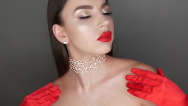 Belle fille modèle avec de grandes lèvres peintes avec du rouge à lèvres rouge. Jeune femme posant dans des gants rouges élégants et lumineux maquillage du soir, en regardant la caméra — Video