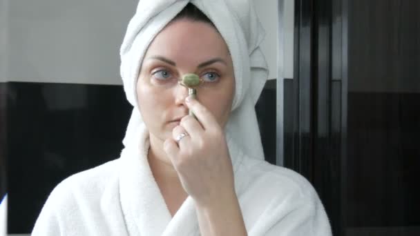 Piękna kobieta z ręcznikiem na głowie robi masaż jadeitowym wałkiem do twarzy mostu nosa z kamienia naturalnego. Chińskie narzędzia piękności. Masaż limfatyczny skóry przed starzeniem się zmarszczek — Wideo stockowe