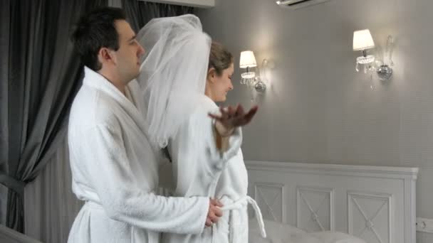 Funny married young newlywed couple dancing merrily in the hotel. Bride in a veil and a white bathrobe with the groom having fun and rejoicing — Stock Video