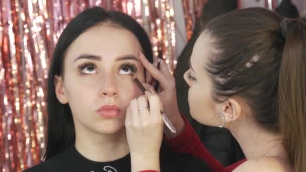 Chica estilista maquillaje artista aplica la fundación bajo la fundación con un cepillo especial en la cara de la chica modelo — Vídeos de Stock