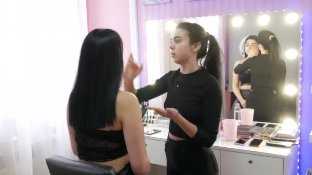 17 maart 2021 - Kamenskoe, Oekraïne: Girl stylist make-up artist brengt stichting onder de stichting aan met een speciale kwast op het gezicht van het modelmeisje — Stockvideo