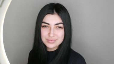 Uzun siyah saçlı, makyajsız kahverengi gözlü güzel bir manken stüdyodaki kameraya bakar ve gülümser.