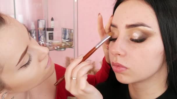 Estilista chica hace un maquillaje brillante con estilo a una joven modelo hermosa mujer en el estudio. Aplica sombra de ojos con un cepillo especial — Vídeos de Stock