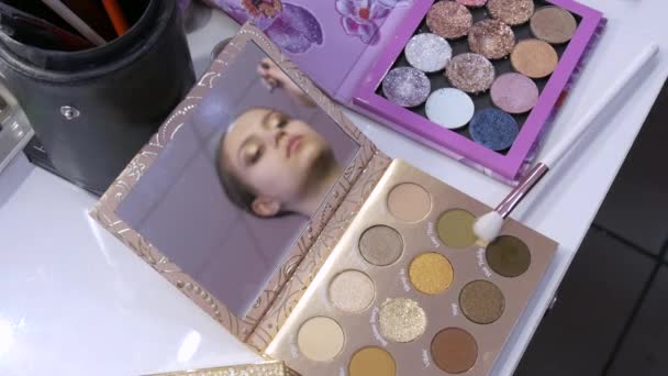 Een interessante weergave van een meisje model tijdens het aanbrengen van make-up, die wordt weergegeven in de spiegel van een peatine met schaduwen — Stockvideo