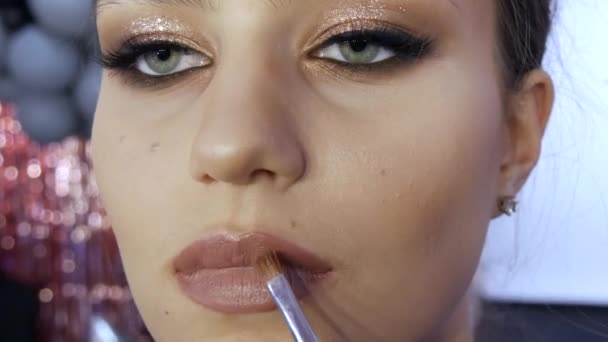 Une brosse spéciale applique un beau rouge à lèvres sur les lèvres d'une jeune fille modèle avec un maquillage élégant et lumineux en soirée — Video