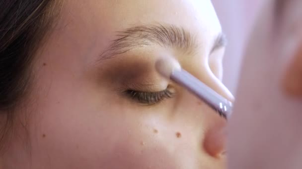 Styliste maquillage maître fait un oeil sur la soirée maquillage lumineux élégant sur un modèle de jeune fille dans un studio de beauté — Video