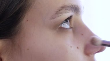 Makyaj ustası, bir güzellik stüdyosundaki genç bir kıza şık, parlak bir makyaj yapıyor. Özel bir fırça kullanarak göz gölgesiyle boyanmış özel bir fırça.