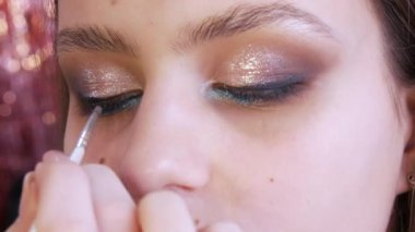 Makyaj ustası bir güzellik stüdyosundaki genç bir kıza şık, parlak bir makyaj yapar. Görüntünün derinliğini vurgulayan ince bir göz kalemi.