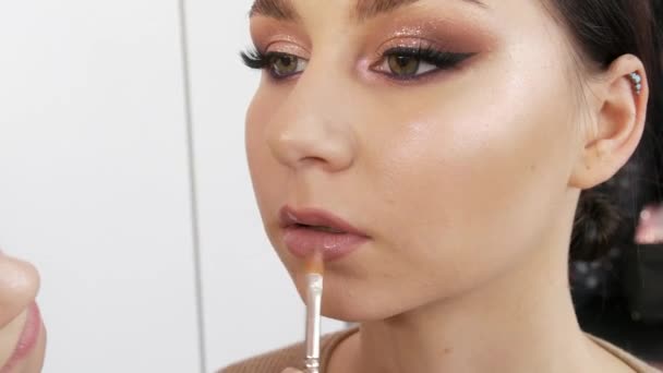 De laatste blik voor de avondmake-up. Het aanbrengen van lippenstift op de lippen van een mooi jong meisje model met een borstel — Stockvideo