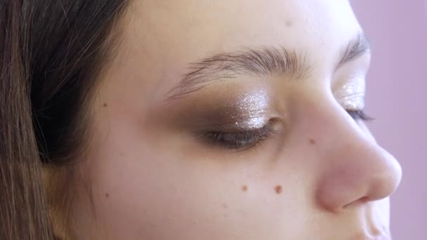A stylist make-up mester teszi a szemét az esti elegáns fényes smink egy fiatal lány modell egy kozmetikai stúdió, egy speciális ecset festékek szemhéjfesték segítségével egy speciális ecset — Stock videók