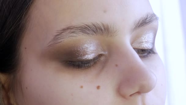 A stylist make-up mester teszi a szemét az esti elegáns fényes smink egy fiatal lány modell egy kozmetikai stúdió, egy speciális ecset festékek szemhéjfesték segítségével egy speciális ecset — Stock videók