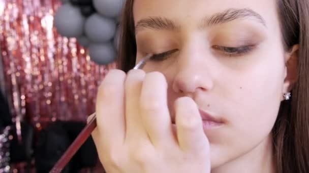 De stylist make-up master maakt een oogje op de avond stijlvolle heldere make-up op een jong meisje model in een beauty studio, een speciale borstel verf met oogschaduw met behulp van een speciale borstel — Stockvideo