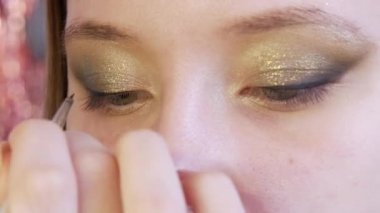 Makyöz, modellere özel bir fırça kullanarak göz makyajı yapar. Siyah, ince göz kalemi görüntünün derinliğini vurgulamak için göz boyunca düz bir çizgi oluşturur.