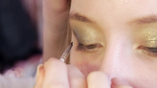 El maquillador hace que los modelos de maquillaje de ojos utilizando un cepillo especial. Negro, delgada delineador de ojos crea una línea recta a través del ojo para enfatizar la profundidad de la mirada — Vídeos de Stock