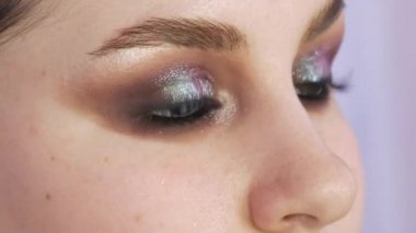 Parlak dumanlı göz makyajlı genç bir kadın modelin güzel anlamlı gözleri. Kendini adamış makyaj fırçası göz alıcı koyu bir bukalemun göz farı sürmektedir.
