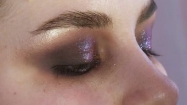 Parlak dumanlı göz makyajlı genç bir kadın modelin güzel anlamlı gözleri. Kendini adamış makyaj fırçası göz alıcı koyu bir bukalemun göz farı sürmektedir.