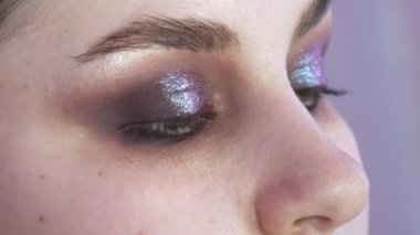 Parlak dumanlı göz makyajlı genç bir kadın modelin güzel anlamlı gözleri. Kendini adamış makyaj fırçası göz alıcı koyu bir bukalemun göz farı sürmektedir.