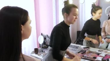 23 Mart 2021 - Kamenskoe, Ukrayna: Makyaj sanatçısı, güzellik stüdyosundaki aynanın önünde modelin yüzüne makyaj yapar. Kozmetik paletleri, rujları, fırçaları, temeli olan masa