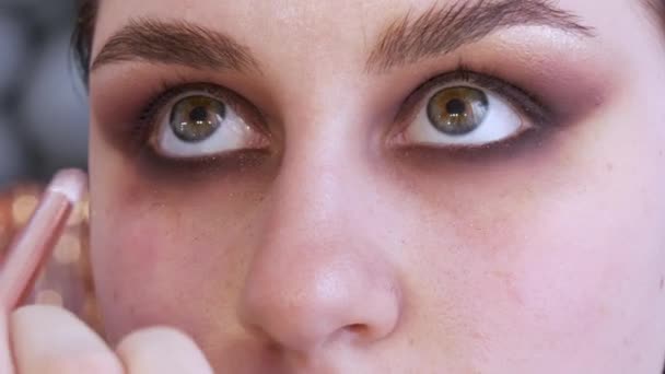 Beaux yeux expressifs d'une jeune mannequin féminine aux yeux fumés et brillants. Ombres sombres sont appliquées avec un pinceau spécial sous les yeux — Video
