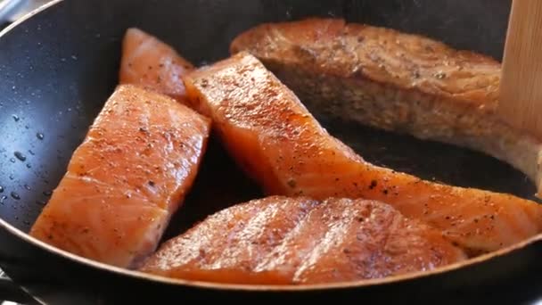 Grote stukjes rode zalmvisfilets worden in een pan gebakken. Houten keukenspatel maakt een stuk rode vis ongedaan — Stockvideo