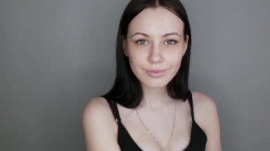 Kameranın önünde poz veren güzel bir manken. Gri arka plana makyaj yapmadan önce makyajsız genç bir kadın.