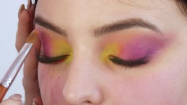 Profesyonel makyöz, stüdyodaki göz kapaklarında sarı ve pembe göz farı modelleri için parlak moda makyajı yapar.