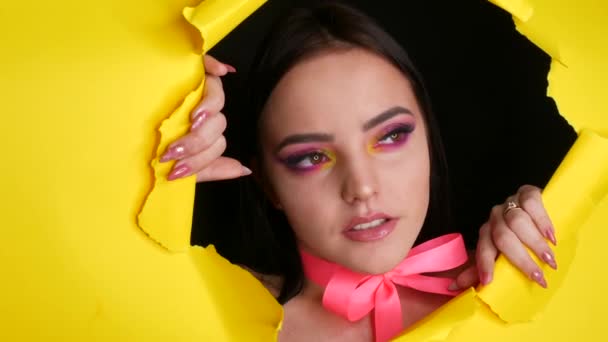 Un beau modèle de jeune fille avec un maquillage de mode jaune juteux lumineux et un arc rose autour du cou sur un fond de papier jaune élégant. Image modèle de mode — Video
