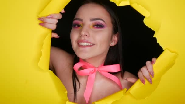Красива модель молодої дівчини з яскравим соковитим жовтим модним макіяжем і рожевим бантом навколо шиї на фоні стильного жовтого паперу. зображення моделі моди — стокове відео