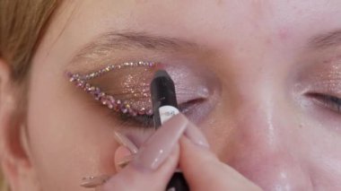 Profesyonel bir makyöz, genç ve güzel bir mankenin göz ve göz kapaklarına özel yapay elmaslar takar. Parlak moda yakın çekim görüntüsü