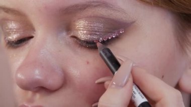 Profesyonel bir makyöz, genç ve güzel bir mankenin göz ve göz kapaklarına özel yapay elmaslar takar. Parlak moda yakın çekim görüntüsü