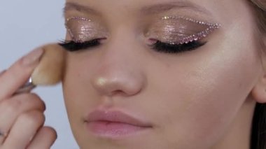 Profesyonel bir makyöz, genç ve güzel bir mankenin yüzüne özel bir fırçayla kapatıcı allık sürer. Sahte elmaslar ve pembe göz kalemleriyle ışıldayan moda.