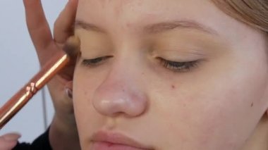 Profesyonel bir makyöz, özel bir fırçayla genç ve güzel bir kızın yüzüne göz makyajı altında bir taban uygular.