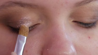 Profesyonel bir makyöz, genç ve güzel bir kız model için özel bir fırçayla çıplak bir gölgede parlak bir göz farı sürer.