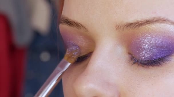 Hermosas sombras brillantes violeta-lila se aplican con un cepillo especial en el párpado del modelo. El proceso de maquillaje de noche brillante vista de cerca — Vídeos de Stock