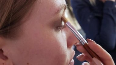 Güzel, parlak gölgeler modelin göz kapağına özel bir fırçayla uygulanır. Parlak akşam makyajı süreci yakın çekim görüntüsü