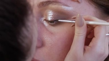Güzel, parlak gölgeler ve göz kalemi modelin göz kapağına özel bir fırçayla uygulanır. Parlak akşam makyajı süreci yakın çekim görüntüsü
