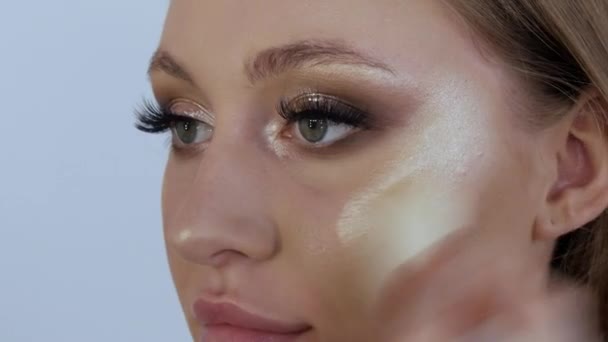 The highlighter is applied to the cheekbones of a beautiful young female model using a special thick brush. Professional make-up at the makeup artists stylist in the studio — 图库视频影像