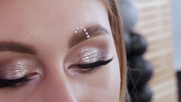 Professional stylist make-up artist makes bright fashion makeup, sticks special multi-colored rhinestones on the eyebrow — 图库视频影像