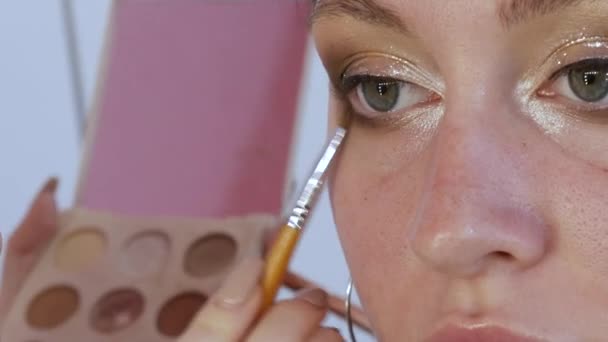 Schöne glänzende Schatten werden mit einem speziellen Pinsel auf das Augenlid des Modells aufgetragen. Der Prozess der hellen Abend Make-up Nahaufnahme — Stockvideo