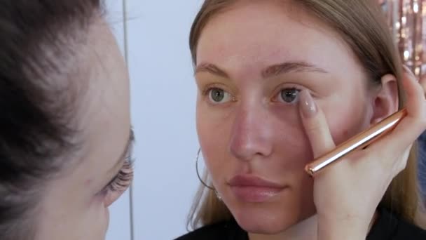 Un cepillo de maquillaje especial aplica una capa de base o corrector a la cara de los modelos para suavizar el tono de la piel. Maquillaje profesional — Vídeos de Stock