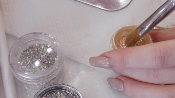 Un ensemble de différents strass pour le maquillage dans des pots spéciaux sur la table chez le maquilleur styliste. La brosse à maquillage ramasse des fards à paupières beige brillant. — Video