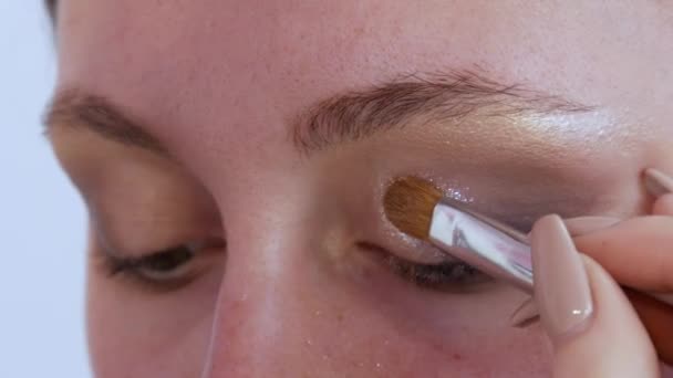 Beautiful shiny shadows are applied with a special brush on the eyelid of the model. The process of bright evening make-up close up view — 图库视频影像