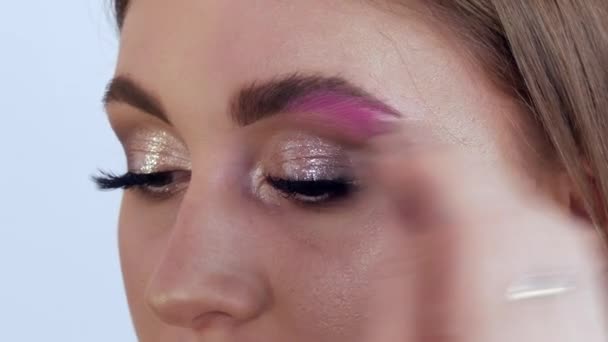 En professionell makeup-artist med en speciell borste korrigerar och målar formen på ögonbrynen på en ung vacker flickmodell. Lysande mode make-up — Stockvideo