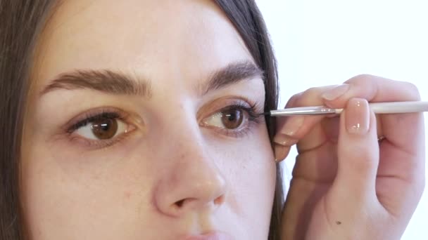 Flicka stylist make-up artist tillämpar en tunn linje av svart eyeliner på glänsande make-up i guld toner på modellerna ögat, närbild — Stockvideo