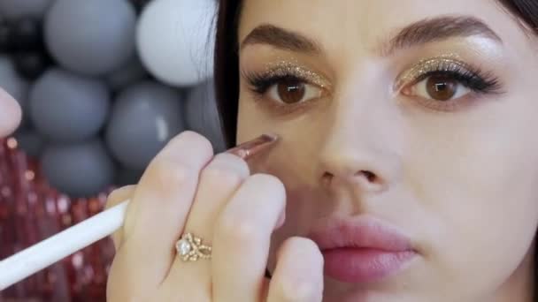 Cepillo aplica la base a la cara de un hermoso modelo joven para el maquillaje de noche ojos ahumados — Vídeos de Stock